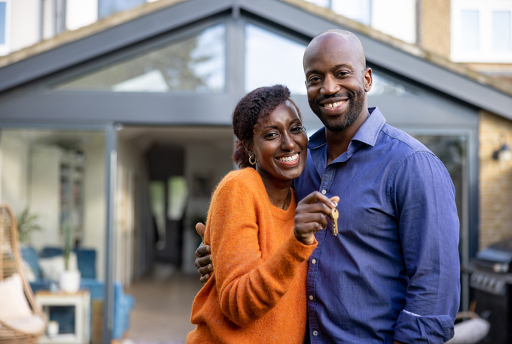 Portrait of a happy black couple holding the keys of their new house and looking at the camera smiling - real estate concepts